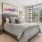  Bedroom with large windows, featuring a gray upholstered bed with geometric-patterned pillows and a throw blanket, mirrored nightstands with lamps, and natural light coming through the windows