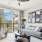 A bright living room at Vista Wilde Lake featuring a gray sofa, modern decor, large windows with patterned curtains, and a view of the balcony and trees outside