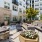 An outdoor courtyard at Vista Wilde Lake featuring lounge seating, dining tables, and planters with flowers, surrounded by modern apartment buildings and greenery