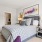 Well-lit bedroom with a gray upholstered bed, geometric-patterned pillows, a throw blanket, mirrored nightstands with lamps, and a large window letting in natural light
